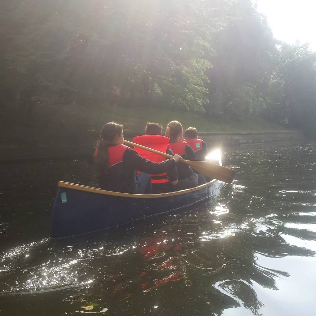Vier Kinder padeln in einem blauen Kanu über den See. Inklusive Stadtcamper des Indiwi Berlins.