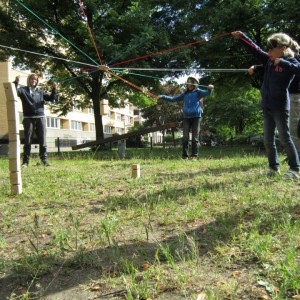 Drei Kinder spannen ein Netz aus Seilen über einen Holzstapel. Indiwi Berlin.