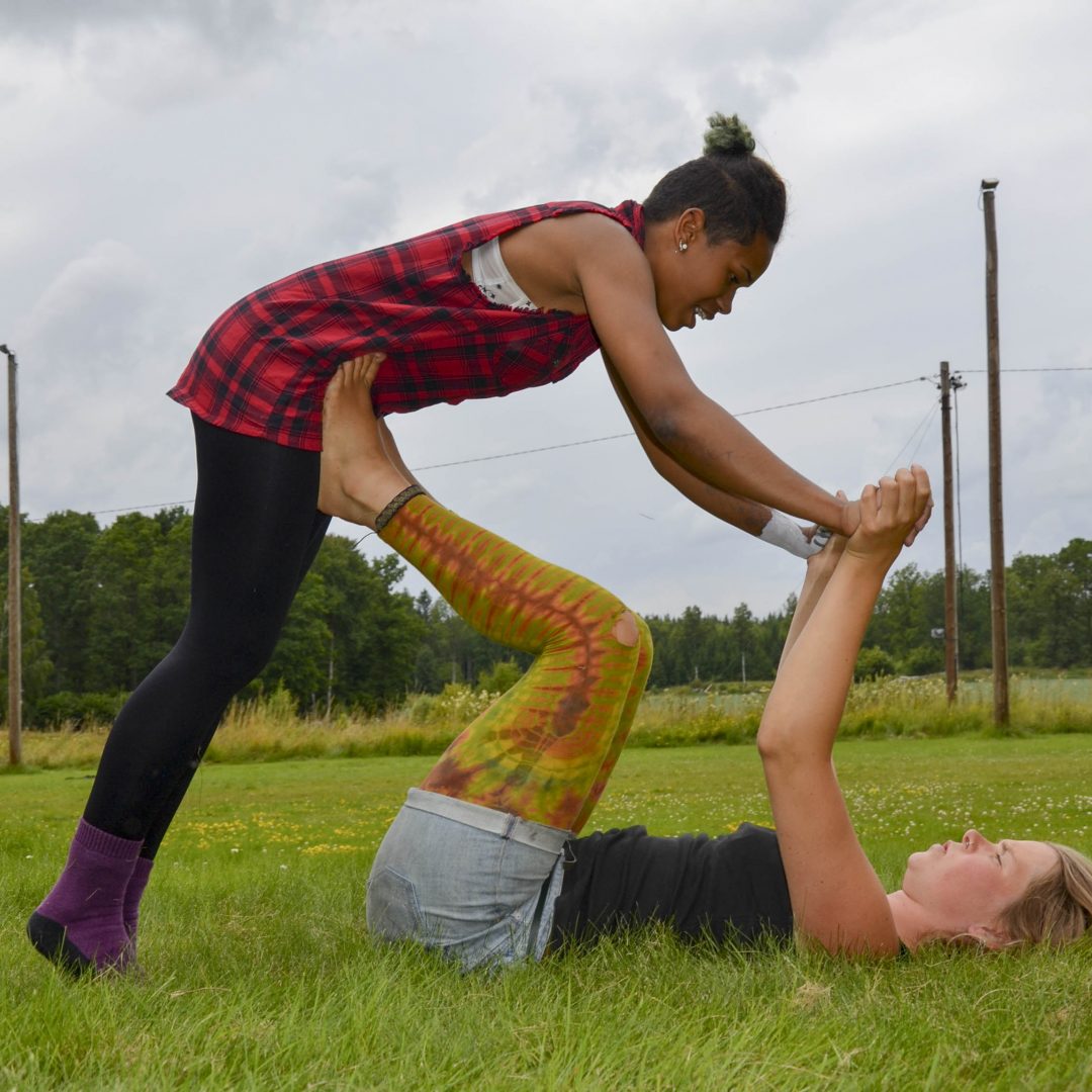 Eine Jugendliche liegt auf der Wiese und streckt Arme und Beine nach oben. Eine andere Jugendliche stützt sich auf ihre Arme und Beine. Inklusive Sommerreise des Indiwi Berlins.