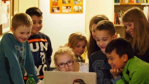 Mehrere Kinder stehen um einen Laptop herum. Sie lachen. Inklusives Medienprojekt des Indiwi Berlins.